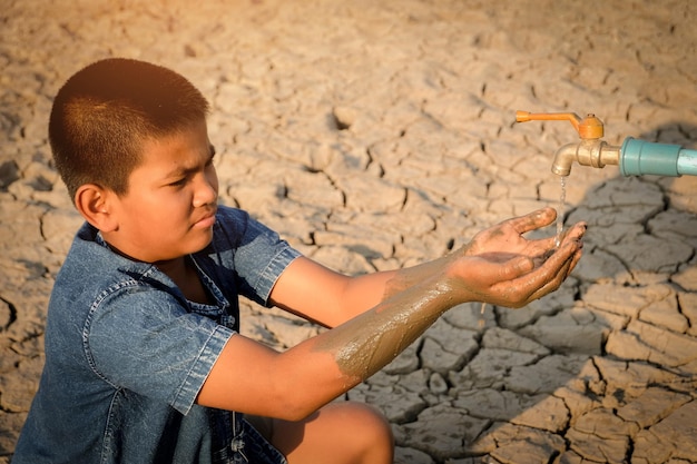 Niño con las manos cubiertas bajo el grifo en la tierra seca