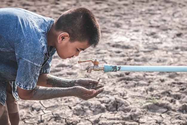 Niño con las manos sucias bajo el grifo en la tierra seca