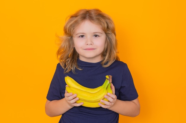 Niño mantenga plátano en estudio Retrato de estudio de niño lindo niño con plátanos aislado sobre fondo amarillo copia espacio