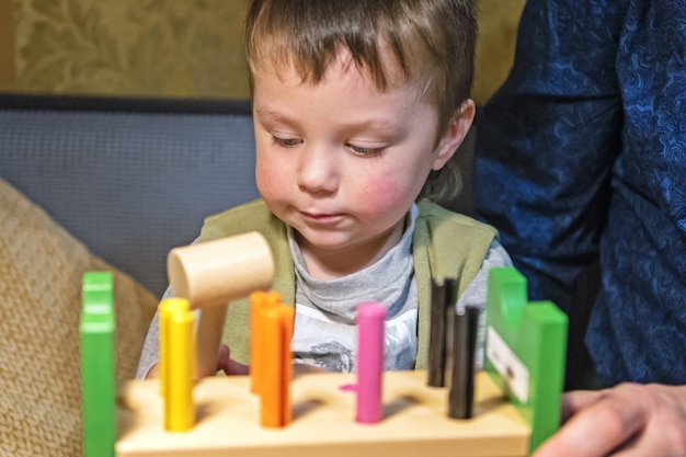 Niño martillando clavos de juguete en una tabla de madera con un martillo