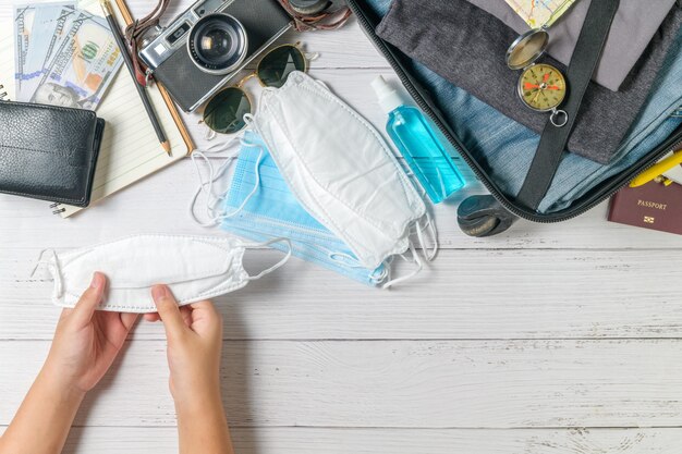 Niño con máscara y maleta, cámara vintage, cuaderno, mapa en madera blanca y espacio de copia. viajar y prevenir el concepto covid 19