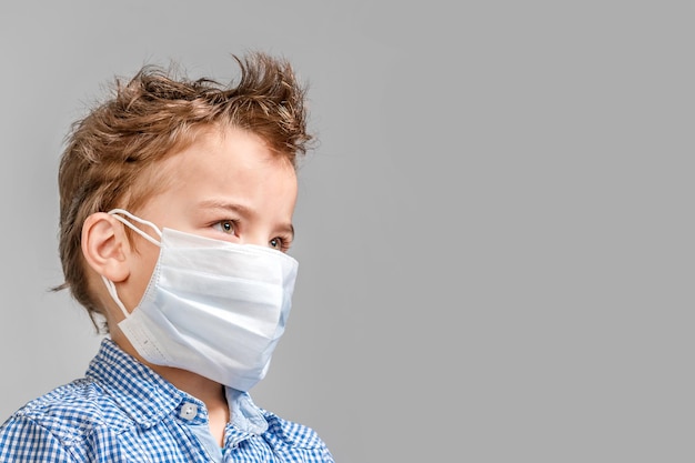 Niño con una máscara médica en la cara sobre un fondo gris aislado
