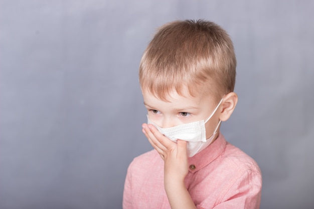 Niño con una máscara médica se cubre la boca con la mano