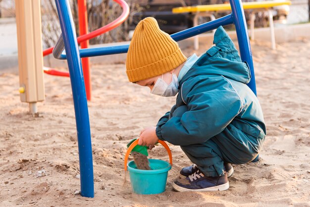 Un niño con una máscara médica juega en el patio de juegos durante la pandemia de coronavirus y Covid - 19