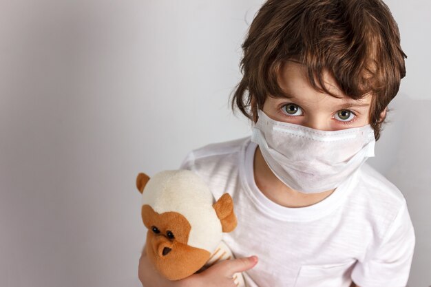 Foto niño en máscara médica con mono de juguete