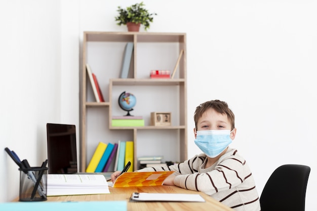 Niño con máscara médica posando mientras hace la tarea