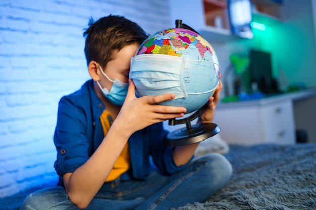 Un niño con una máscara médica sostiene un globo terráqueo. El niño cura el planeta. Concepto de contaminación atmosférica y ambiental.