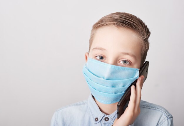 Niño en máscara médica con teléfono móvil. Concepto de coronavirus y contaminación del aire pm2.5. Síntomas del virus Concepto de epidemia, gripe, protección contra enfermedades, vacunación. Enfermedad de la gripe. Atención médica.