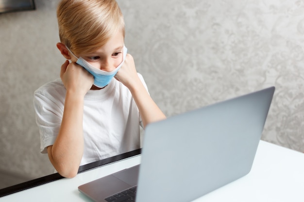 un niño con una máscara médica trabaja en una computadora