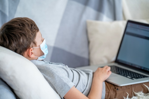 Niño con mascarilla usando la computadora para la tarea