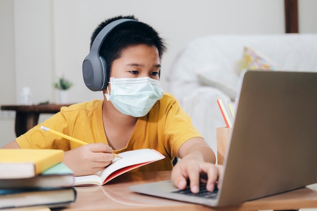 Niño con mascarillas estudio en línea en casa.