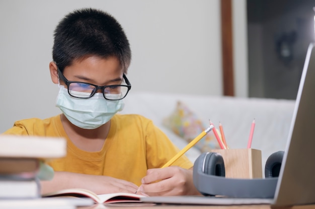 Niño con mascarillas estudio en línea en casa.