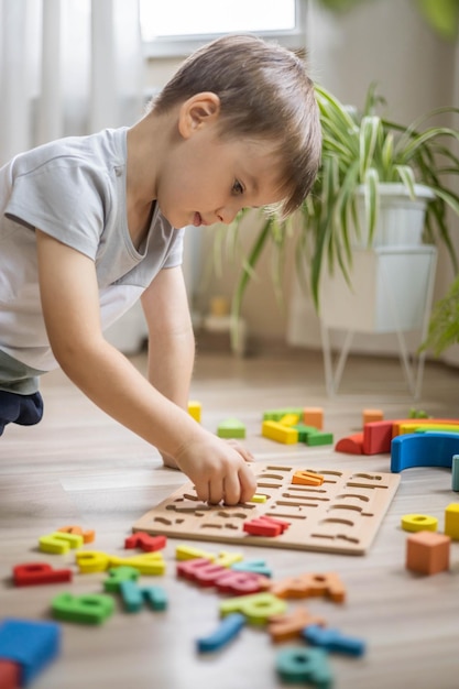 Niño masculino jugando con letras del alfabeto ecológico de madera en la mesa vista del juego intelectual