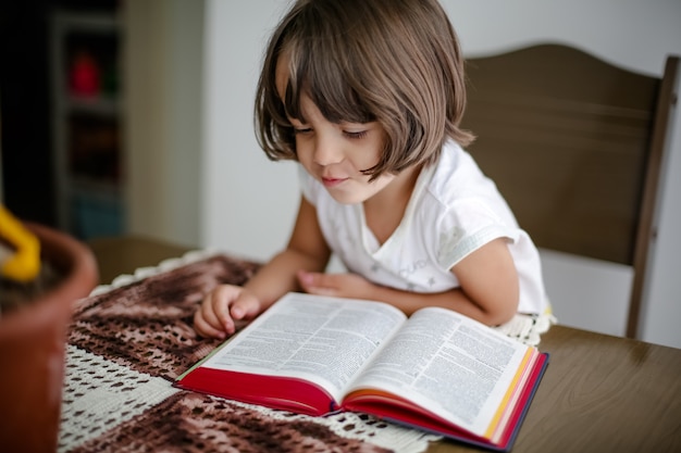 Niño en la mesa leyendo la Santa Biblia y hojeándola