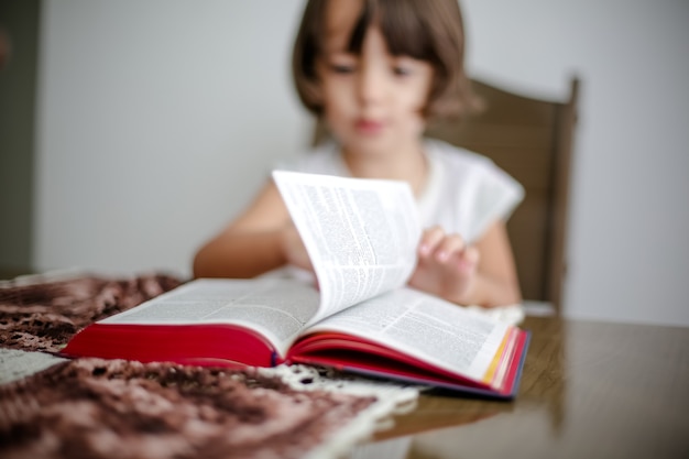 Niño en la mesa leyendo la Santa Biblia y hojeándola