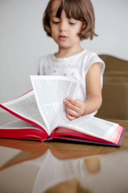 Niño en la mesa leyendo la Santa Biblia y hojeándola