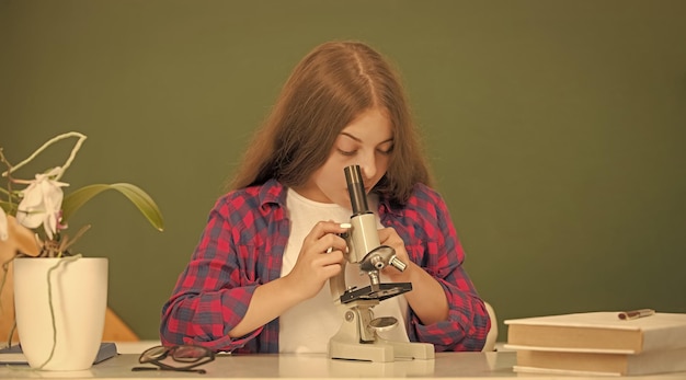 Niño con microscopio en el aula en la ciencia de la pizarra