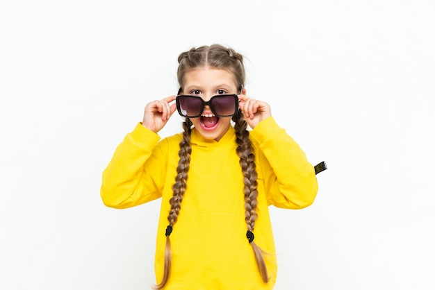 El niño mira por debajo de las gafas de sol Una hermosa niña con un traje de verano amarillo sobre un fondo blanco aislado