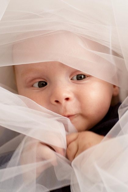 un niño mira a través de la tela. tela blanca retrato del bebé. el niño de ojos azules