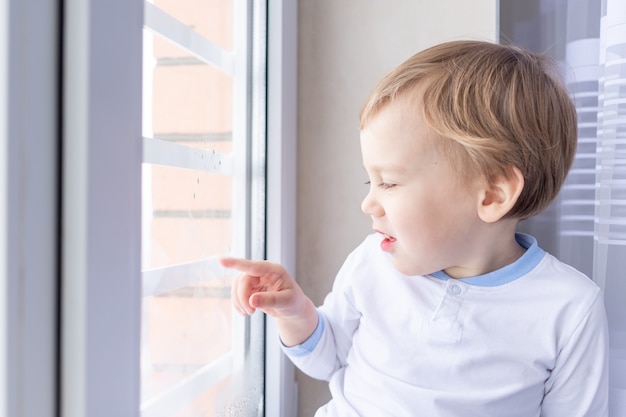 Un niño mira por la ventana sentado en el alféizar de la ventana de la casa