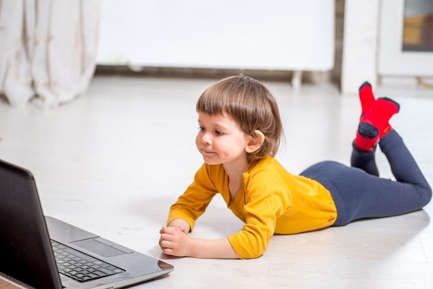 Niño mirando una computadora portátil mientras está acostado en un piso claro en casa