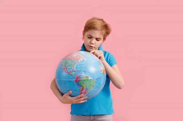 Niño mirando un globo contra un fondo rosa