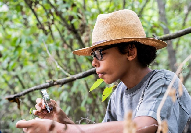 Foto niño mirando una hoja con una lupa buscando el micromundo de la naturaleza concepto de naturaleza y medio ambiente adolescente amante
