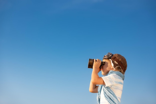 Niño mirando a través de binoculares contra el cielo azul Niño divirtiéndose al aire libre en verano Concepto de viaje y aventura