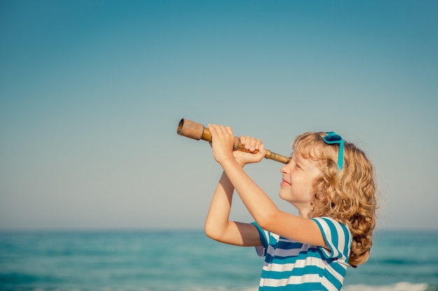 Niño mirando a través del catalejo contra el fondo del cielo y el mar