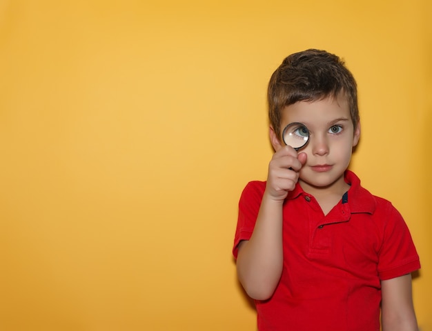Foto niño mirando a través de una lupa sobre fondo amarillo. espacio para texto