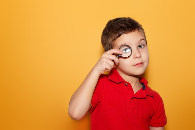 Niño mirando a través de una lupa sobre fondo amarillo. Espacio para texto