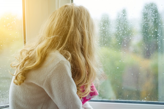 Niño mirando en una ventana de otoño con gotas de lluvia