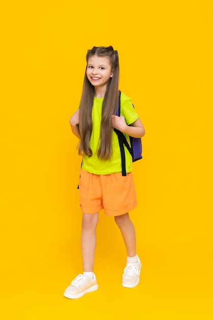 Un niño con una mochila de cuerpo entero Una niña con una cartera en pantalones cortos Clases educativas adicionales de verano para niños Preparación para el año escolar Fondo amarillo aislado