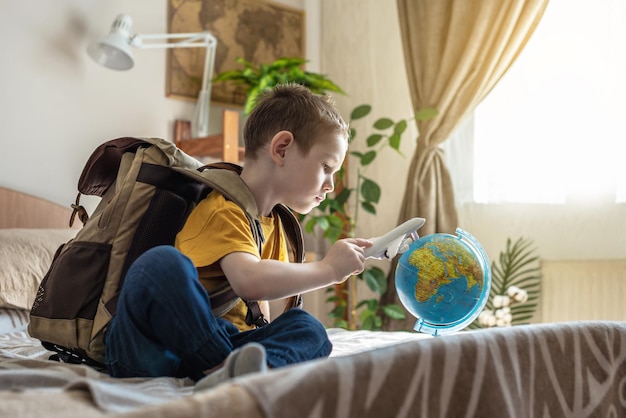 Un niño con mochila está jugando con un avión de juguete y un globo terráqueo yendo en un viaje hacia la aventura