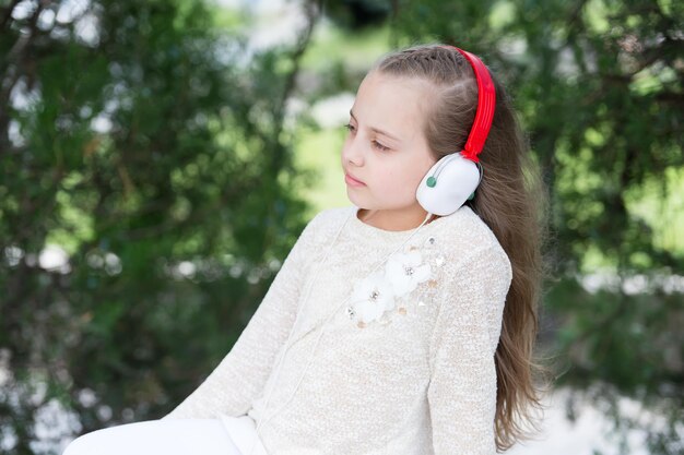 Niño de moda y tecnología moderna Sonido de melodía y mp3 Niña escucha música en el parque de verano Niño disfruta de música en auriculares al aire libre Vacaciones de verano descanso y diversión