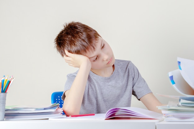 Niño molesto hojear un libro mientras hace la tarea en casa