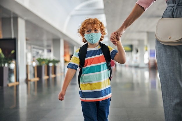 Niño molesto con mochila sosteniendo una mano