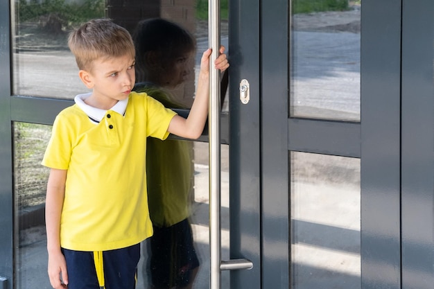 Un niño molesto que se aferra a la manija de la puerta no puede abrir la puerta El niño regresa a casa