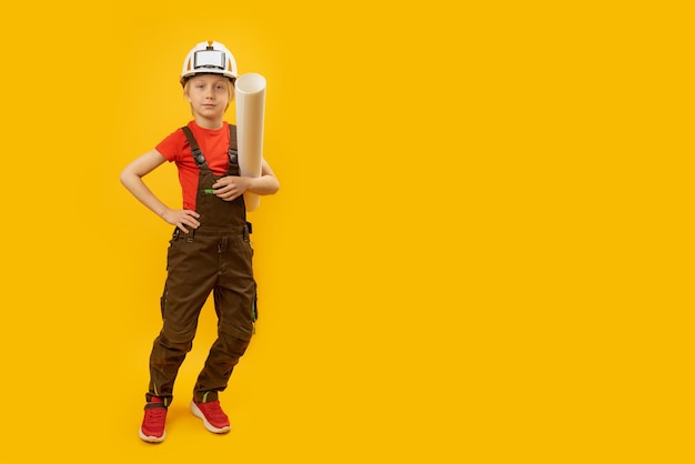 Niño con mono de casco protector y con una hoja de papel en las manos Maqueta de espacio de copia Niño como constructor o arquitecto