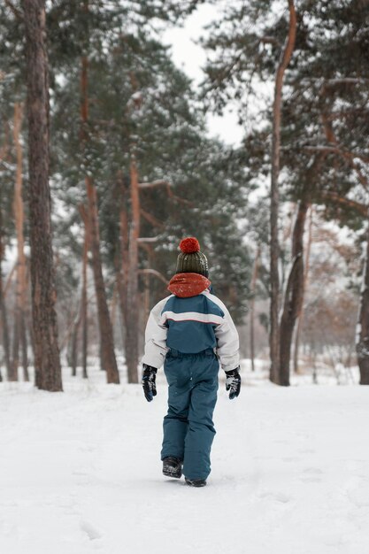 Niño en mono de invierno camina en el bosque en la nieve. Vista trasera. Vacaciones de invierno en el bosque de abetos.