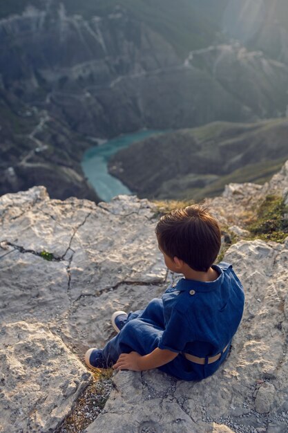 Niño con un mono de lino azul sentado en el acantilado del cañón de Sulak en Daguestán y piensa en la vida