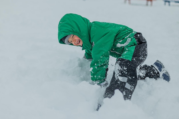 Un niño con un mono verde cayó a la nieve, el niño juega en la nieve, el niño juega afuera en invierno.