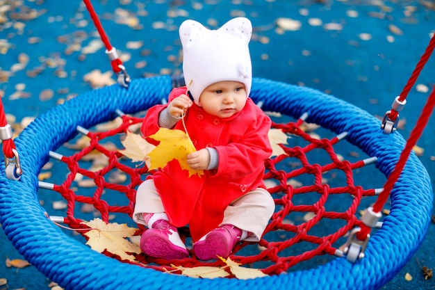 Niño monta en columpio con hojas amarillas de otoño