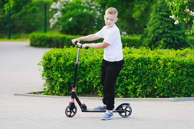 Un niño monta una scooter en el parque en verano. Foto de alta calidad