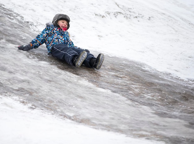 Niño monta en un tobogán de hielo Niño alegre en el invierno