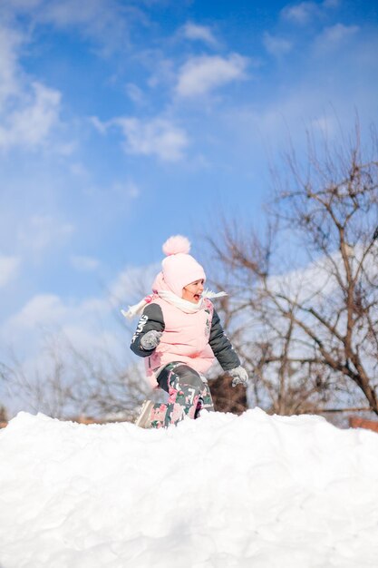 Niño monta en tobogán de nieve niña en traje cálido de invierno juega al aire libre y disfruta de un día soleado en ...