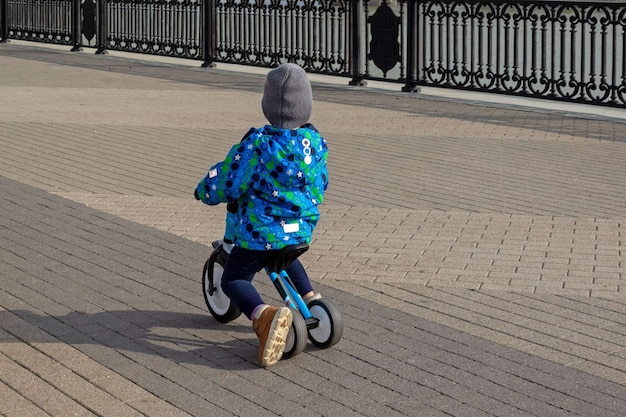 Niño montando una bicicleta de equilibrio en una acera de la ciudad