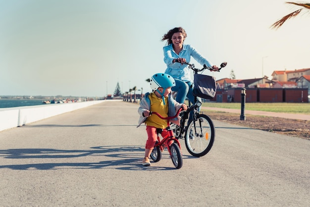 Niño montando una bicicleta de equilibrio con su madre en bicicleta en un parque de la ciudad