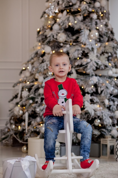 Niño montando un caballo de cartón cerca del árbol de Navidad.