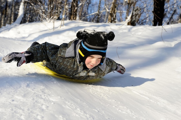 Niño montando con colinas en trineos en clima invernal